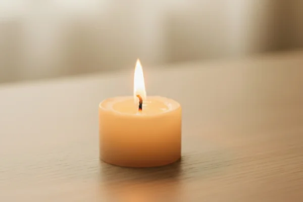 Kleine Kerze brennt ruhig auf hellem Holz, sanftes Licht füllt den Raum