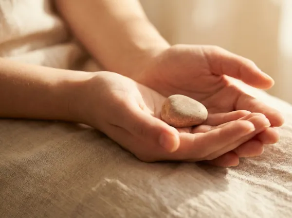Geöffnete Hände halten einen kleinen Stein im warmen Licht, eine ruhige Geste der Sammlung und inneren Klärung.